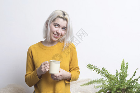 吸引人的快乐年轻女士拿着一杯茶或咖啡带着一束温暖的笑容看着摄影机喜气洋手图片