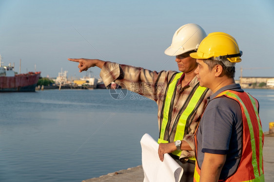 黑色的咨询住房两名工程师站在码头着身安全头盔持有蓝图并参考施工构想中的计划即高效施工管理程概念AC54970图片