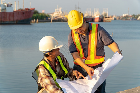 住房两名工程师站在码头着身安全头盔持有蓝图并参考施工构想中的计划即高效施工管理程概念AC54970力量劳动者图片