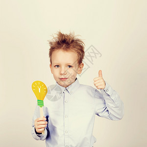 吃惊黑板电灯泡带着黄色纸质灯泡的可爱男孩在一个白色背景的小学生大拇指手持玩具灯泡时拿着玩具灯泡笑着的可爱男孩带着有趣的照片道具孩图片