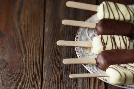 盘子棒上的牛奶巧克力冰棒木制背景板上覆盖着白色和黑巧克力的冰淇淋棒文本空间巧克力冰淇淋棒坚果冰淇淋甜点木制的寒冷图片