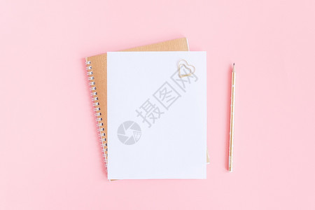 螺旋金色记事本上的空白纸与回形针心和粉红色柔背景上的铅笔模拟您文本和设计顶视图平躺最小样式螺旋金色记事本上的空白纸与回形针心和粉图片