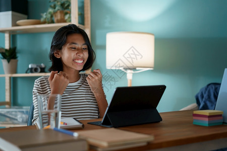 放松知识数字的亚洲小女孩成功通过互联网在数字平板电脑上学习同时坐在家中晚上的办公桌旁儿童快乐和笑在家网上学习的概念YTFEntw图片