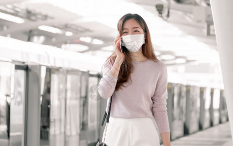 防弹少年团亚裔妇女站在火车工作时身戴面罩及穿衣临时工服在手机上交谈并参加新常态社会分化与交通概念网络疾病图片