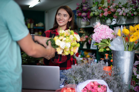 销售量亚洲女花卉小店主她正在使用的电话和笔记本脑为她的商店订单妇女硬木士图片