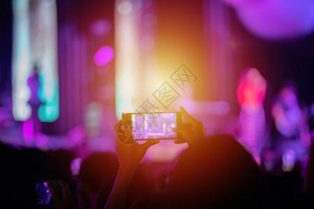 观众举手使用智能机在明亮的舞台灯下拍照和录像校对Portnoyunorg俱乐部鼓掌音图片