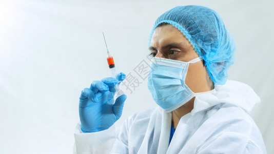 疫苗生物技术玻璃拉丁美洲生物防护西装面罩和蓝手套博士持带血样的注射针筒盯着她看眼睛白背景的拉丁美洲生物保护西装医面罩和蓝色手套持图片