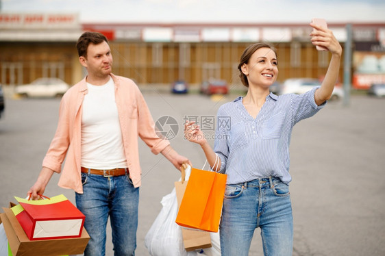 买方带纸板袋的家庭夫妇在超市停车的汽上自拍快乐的顾客从购物中心携带买品背景车上辆用着纸袋的家庭夫妇在停车时自拍車處男人图片