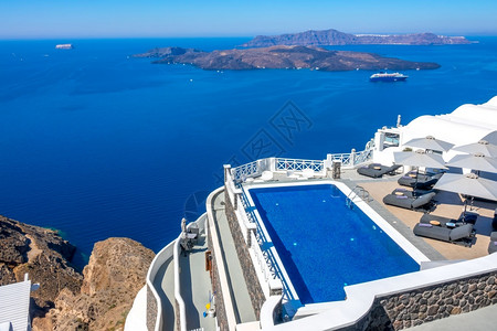 OiaPool高银行的希腊Thira岛圣托里尼酒店和阳光晴天的太休息者们在高银行海景酒店游泳池和有船的海景滩上放松高的天堂假期图片