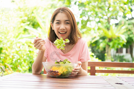女坐在花园旁边房子阳台上吃健康绿色沙拉的保健和营养食品概念她认为在家庭园圃旁边的露台里生活着一个健康的绿色沙拉一种重量图片