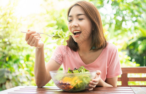 节食吸引人的坐在花园旁边房子阳台上吃健康绿色沙拉的保健和营养食品概念她认为在家庭园圃旁边的露台里生活着一个健康的绿色沙拉饮食图片