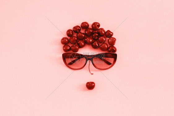 有创造力的红甜樱桃以女在太阳镜中的形象露出粉红背景的嘴唇珊瑚点心概念青年美貌健康饮食或创用平板花朵红甜樱桃在阳光镜中的妇女和粉红图片