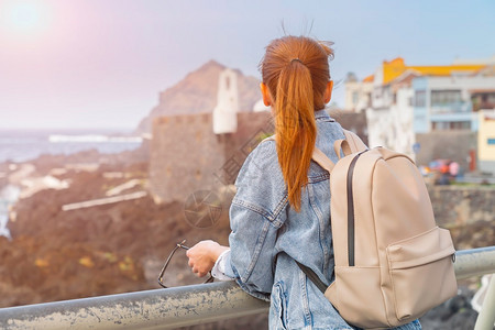背包的红发女孩欣赏位于特內里费岛的加拉奇科的海洋和建筑图片