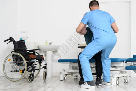 诊所室内的帮助使用轮椅残疾患者在康复医院起床的男物理治疗师高质量照片帮助使用轮椅的残疾患者在康复医院起床的男物理治疗师在职的图片