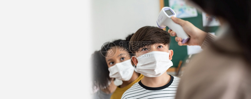 亚洲人医疗查看使用数字温度计对亚裔男孩和非洲美国女孩额头进行检查温度测量的教师用数字温度计来检测亚洲男孩和非裔美国女孩的温度在课图片