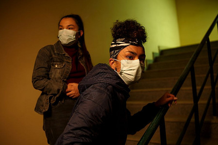 一名身着次医疗保护面罩的亚洲和非年轻女孩躲在楼梯井上避感染的人从感染中解救出跨种族的国际援助友谊和救a一名身着次医疗保护面罩的亚图片