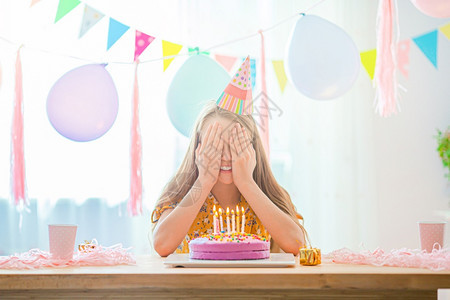 快乐的小女孩在生日派对上许愿希望白种女孩满怀梦想地微笑看着生日彩虹蛋糕喜悦的多彩背景气球生日派对和愿望的概念YLAK停留帽内部的图片