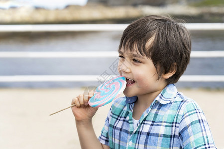 年轻的关心有趣小孩吃棒糖快乐的小男孩拿着大糖果孩子笑脸的吃甜食活跃的童年在阳光明媚的夏日享受户外游乐公主图片