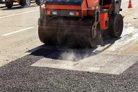 路面修理沥青表的热天气晴明道路上要修理的一条重振动式滚轴压公路沥青需要修理的材料筑路工清除铺设图片