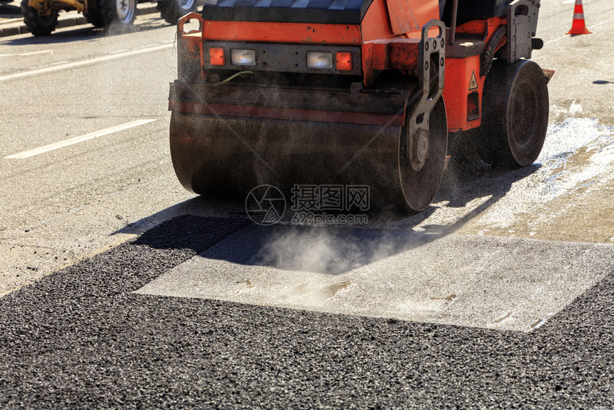 路面修理沥青表的热天气晴明道路上要修理的一条重振动式滚轴压公路沥青需要修理的材料筑路工清除铺设图片