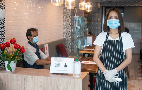 保持疾病身戴面罩和持有红外前额温度计的亚洲女服务员在进入餐馆咖啡店之前检查顾客身上的症状以检查体温在进入餐厅咖啡店之前检查客户的图片