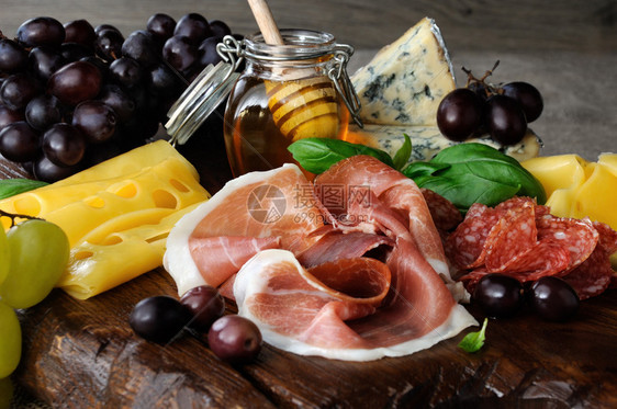 开胃菜用肉干熏香肠腊芝士橄榄和葡萄在木制背景上配菜什锦的一种图片