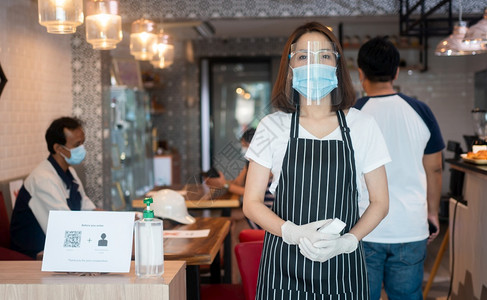 亚洲人零售身戴面罩和持有红外前额温度计的亚洲女服务员在进入餐馆咖啡店之前检查顾客身上的症状以检查体温在进入餐厅咖啡店之前检查图片