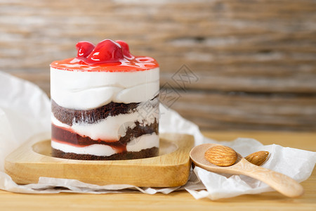 糖果巧克力蛋糕加草莓樱桃和木制餐桌上的白奶油木勺子和杏仁糊棕色的投标图片