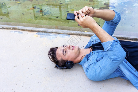 黑耳机青年坐在地板上梦想着在公园用手机度过时间使用手机爱好肖像户外图片