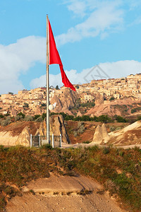 在古老的地下洞穴村庄UchisarCappadocia的背景下土耳其在金属悬崖上挂着巨大的红阳光明日垂直图像空间复制土耳其在卡帕图片