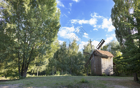 一种座古老的木制风车在青春的森林里一个绿色的草地上面对着一片蓝色的天空和浅白云一座古老的木制风车在夏日的森林里生长农场背景图片
