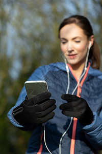 户外锻炼赛跑者年轻女在公园行前选择音乐在移动电话上倾听声音图片