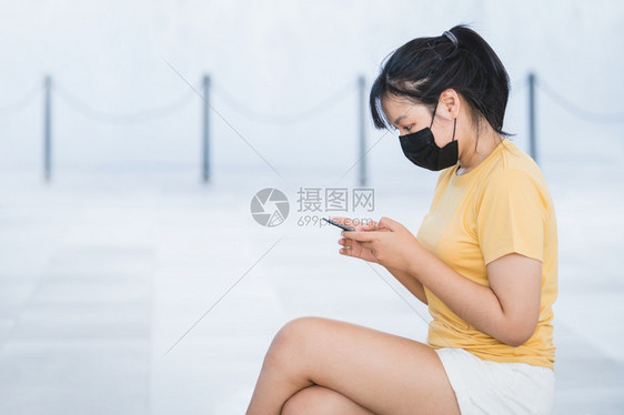 身戴面罩的亚裔妇女坐在社会媒体上浏览社交媒体通过手机更新COVID闻在户外科技与医疗概念新常态下信息城市亚洲人图片