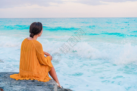 人们海滩日落时的年轻美女后退时看晚上穿着衣服的女孩在海边日落背景的岩石上年轻美丽的女孩魅力图片