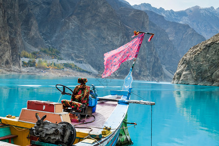 座位在巴基斯坦吉尔特俾提斯坦GojalHunza山谷背景的丘下在绿石阿塔巴德湖停靠着一艘多彩横滨的船旅游石头图片