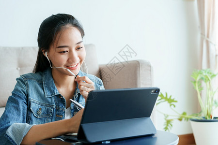 亚洲人会议室工作场所昂亚裔妇女正利用平板电脑与同事举行视会议在家中使用科技术身着牛仔衬衫的美貌女在讨论家用耳机的工作笑声图片