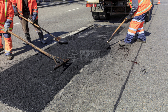 劳动团队道路建筑工作组在公路段分发新鲜沥青并将其平分用于维修工作组在建公路期间平均分配部沥青并有铲子在建造公路期间平均分配部沥青图片
