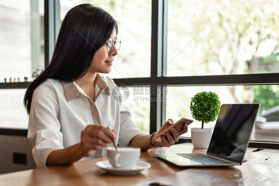金融报告专业的从事笔记本电脑和智能手机工作的商业妇女在办公室喝咖啡的中从事手写笔记本电脑和智能手机的工作以及商务和生活方式概念企图片