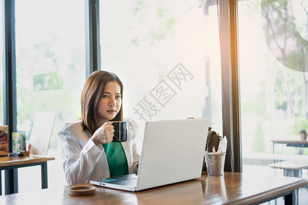 咖啡店业务中与使用计算机和智能手合作的女商人放松和中断自由职业者工作和自由企业融资的成功率在咖啡店商业中从事使用计算机和智能手工图片