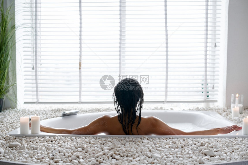 迷人的年轻女在泡浴中放松后视女在浴缸中美容和保健在水疗中心浴室的健康治疗鹅卵石和蜡烛在背景迷人的女在泡浴中放松后视泡沫洗涤白色的图片
