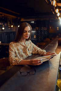 一种女士在酒吧的柜台坐着一本书的漂亮女人一名在酒吧人情休闲活动夜生妇女一本书在酒吧的柜台坐着美丽图片