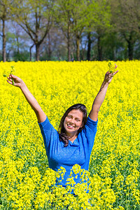 笑快乐的年轻古伦巴女人在盛开的黄色种子田里举起手来春天蓝色的图片