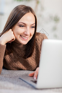 坐在沙发上与电脑聊天的caucasian女人微笑的照片漂亮白种人屋图片
