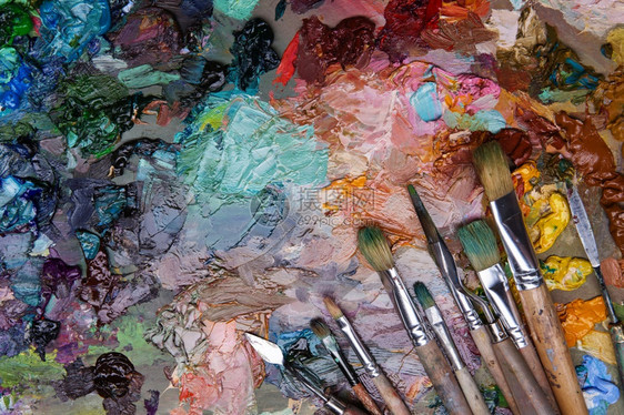 白色的艺术家在木制调色盘上刷子和涂油画大型艺人调味盘不同颜色的质料混合油漆以及用笔和调色板加颜料味各种样的画笔图片