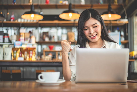 电话亚洲女自由职业妇做出快乐的姿态在咖啡馆使用笔记本电脑时举手商业与成功概念咖啡店和户外主题食堂背景互联网杯子图片