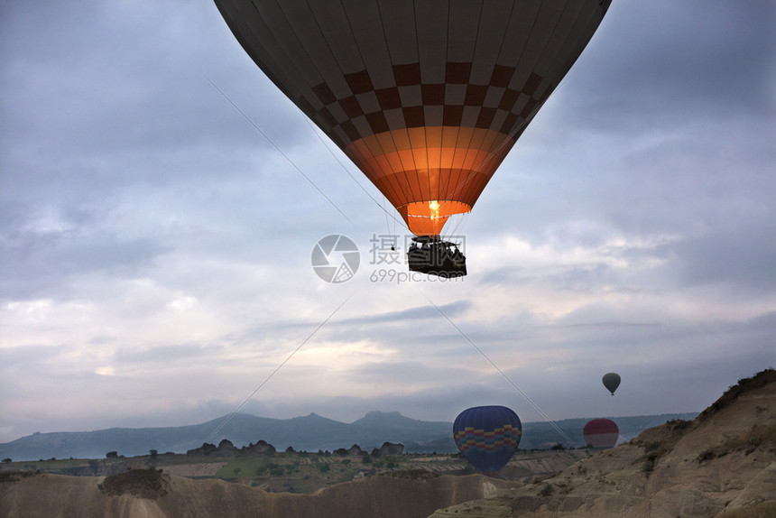 壮观有色岩石A气球正在飞过卡帕多西亚12058土耳其2058日黎明时分在12058年土耳其的卡帕多西亚山谷上空飞行图片