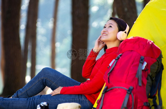 周末野营绿色一位年轻女孩坐在露营帐篷和红背包旁边她喜欢在湖森林中听耳机和欣赏自然的音乐泰国MeeHongSonPangOungM图片