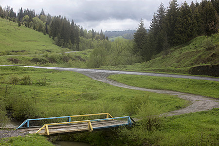 在喀尔巴阡山道路谷一条溪流上横跨座木制老桥在山路谷的一条小溪上穿过Wooden老桥之间草穿越美丽图片