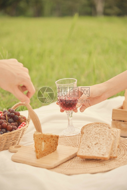 食物草地有人在野餐时给另一个人送杯葡萄汁给另个在野餐中试图拿起面包吃的人吗草图片