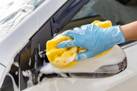戴蓝色手套和黄海绵冲洗侧面镜子现代汽车或清洁洗概念的妇女手蓝套服务店铺红色的图片